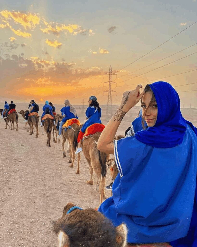 Camel caravan and quad riders in Marrakech desert at sunset