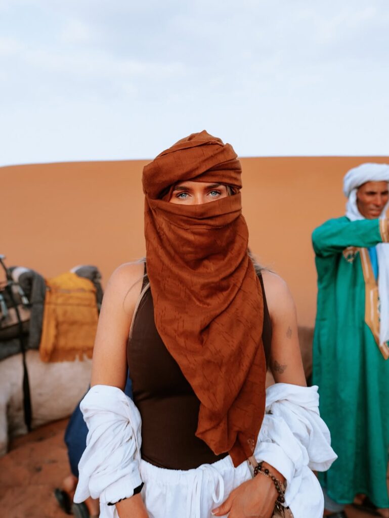 Solo traveler in turquoise robes exploring golden sand dunes in Morocco desert landscape Split image: rocky Zagora desert vs. golden Erg Chebbi dunes in Morocco