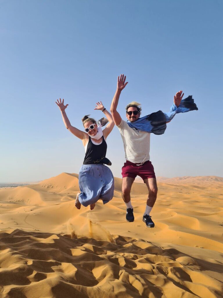 Two happy travelers jumping over golden dunes during Sahara Desert tour from Marrakech