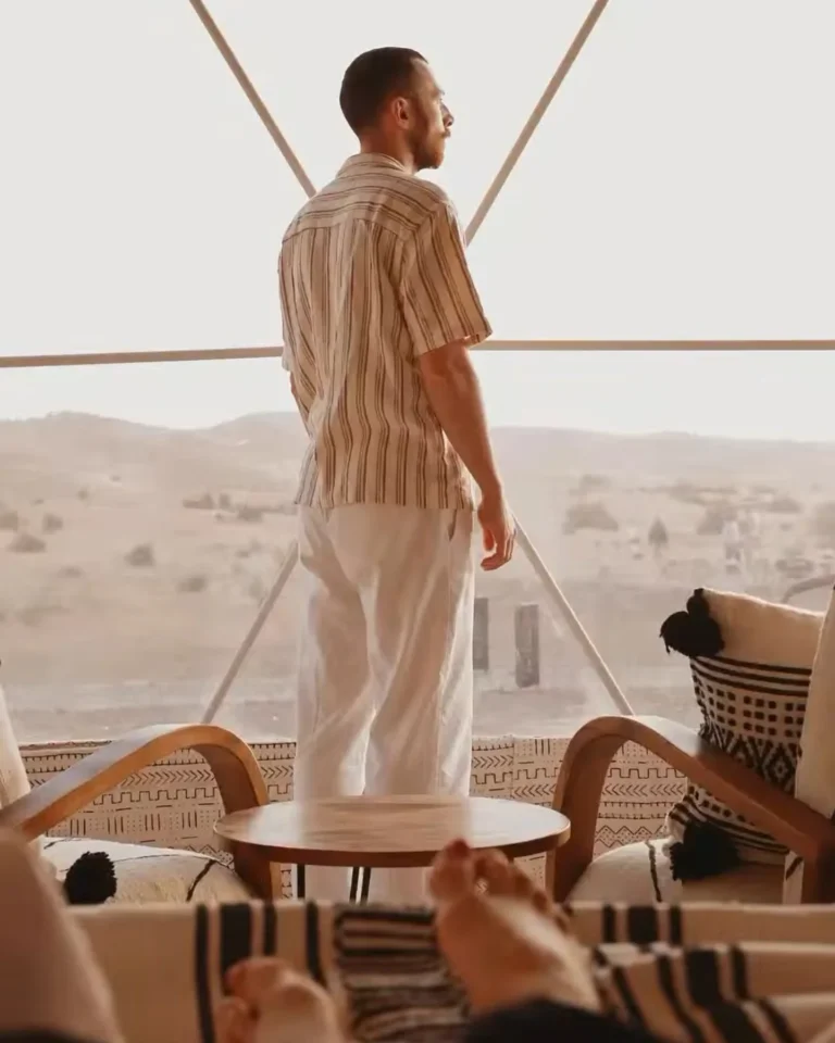 Traveller looking out over the dunes from a glass-walled desert suite