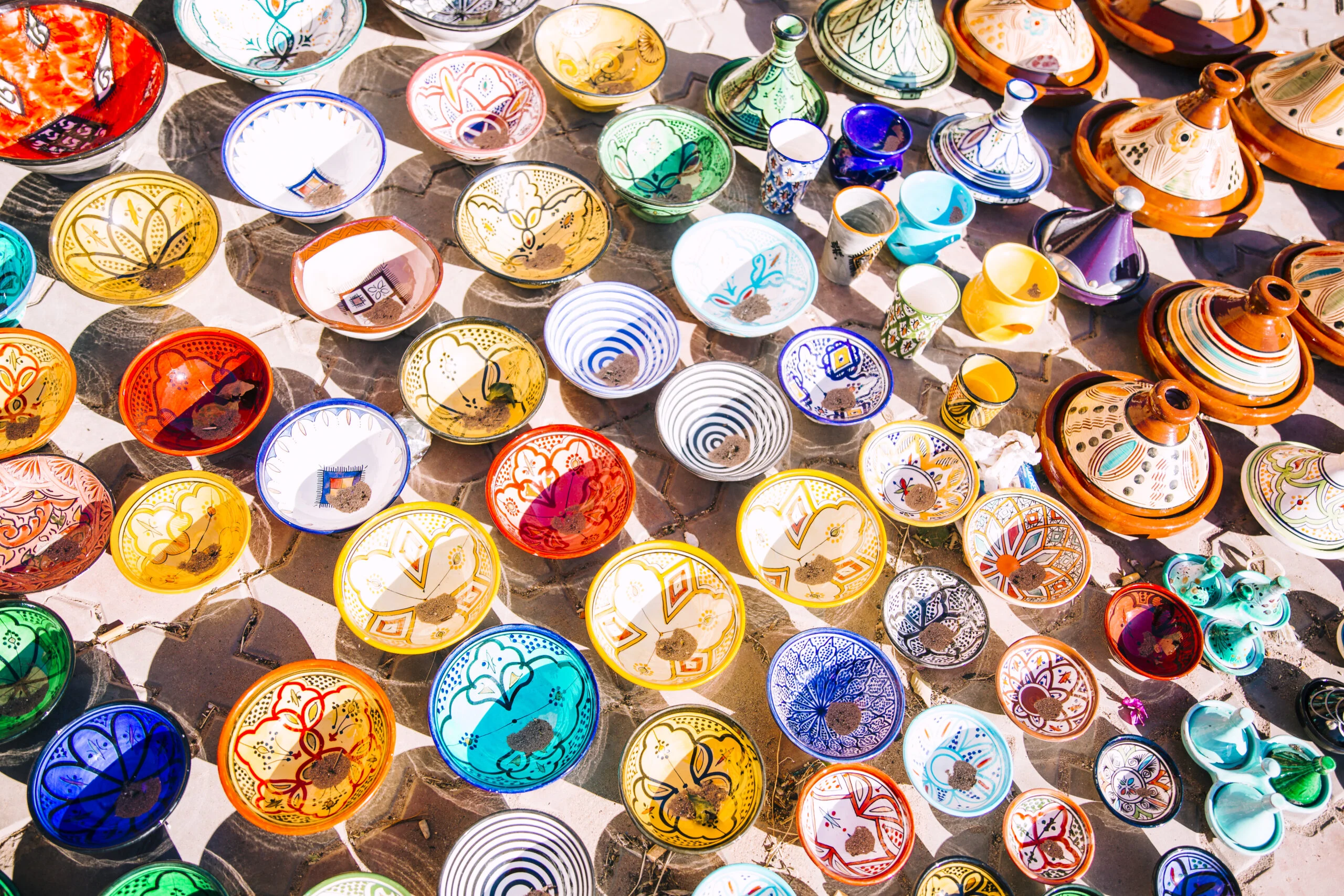 How Much Does a Trip to Morocco Cost? A Real 2026 Budget Breakdown 3 Stacks of colorful hand-painted Moroccan plates and bowls for sale at a market
